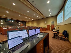 Monitors displaying a presentation in the foreground and students in the background
