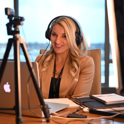 Peggy Coffeen sits at a desk with headphones on in front of a laptop and tripod